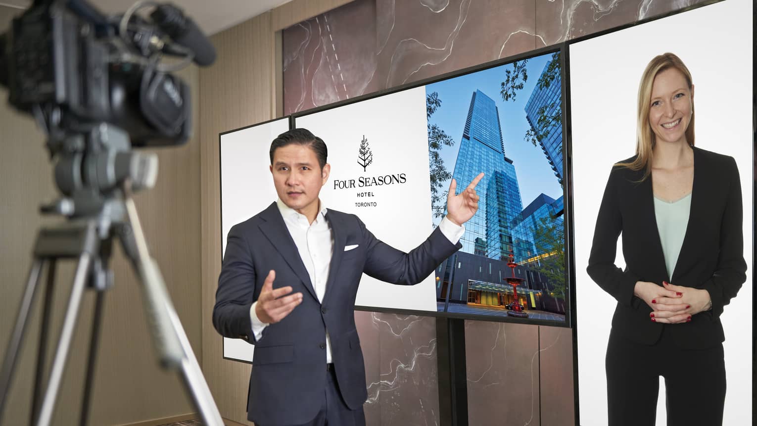 A man in a suit points to a screen as he virtually speaks with a female colleague. 