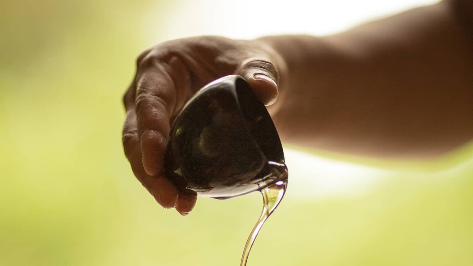 A set of hands pours massage oil from a ceramic bowl into a palm