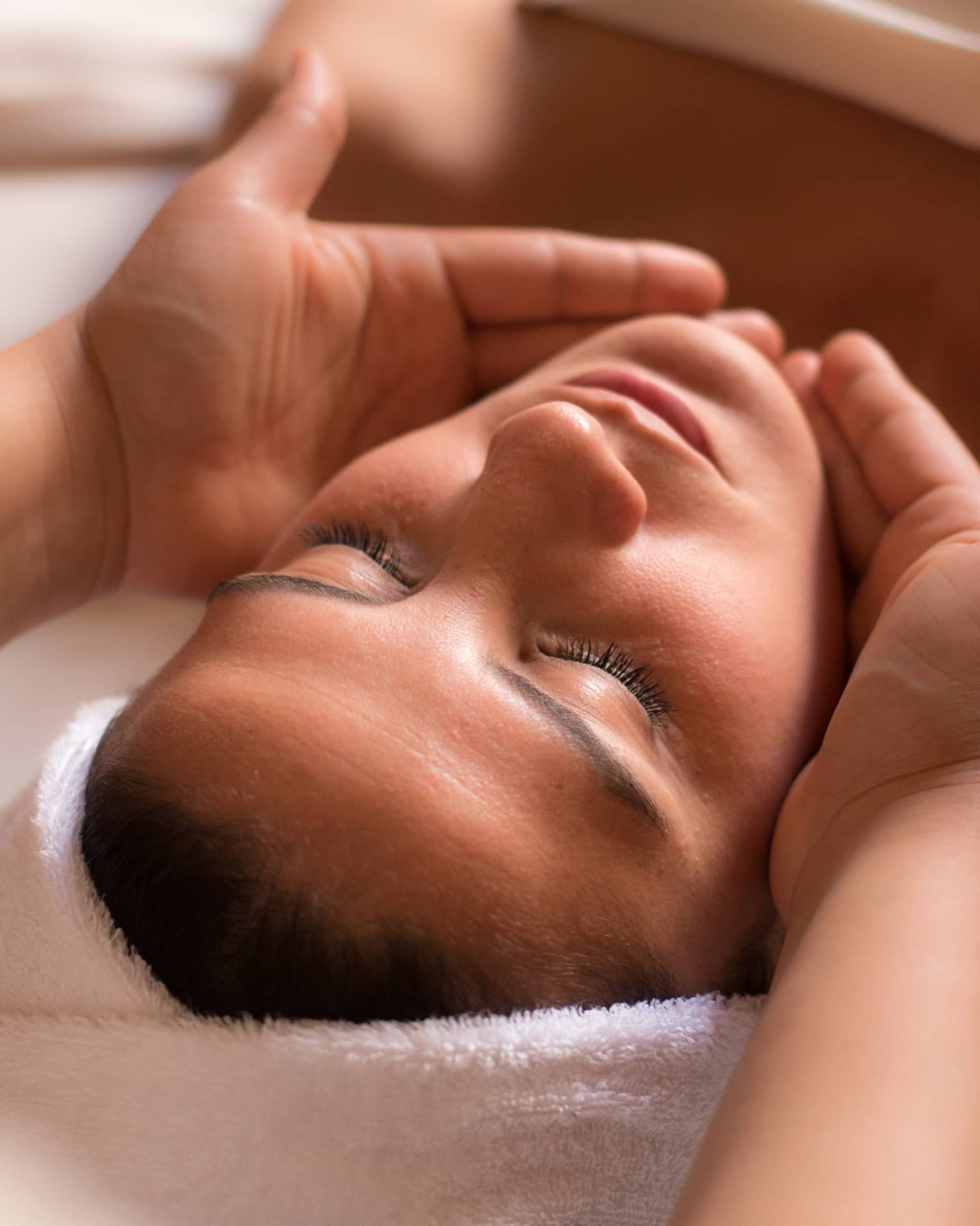 Close-up of woman with eyes closed facing up as hands cup her face and chin