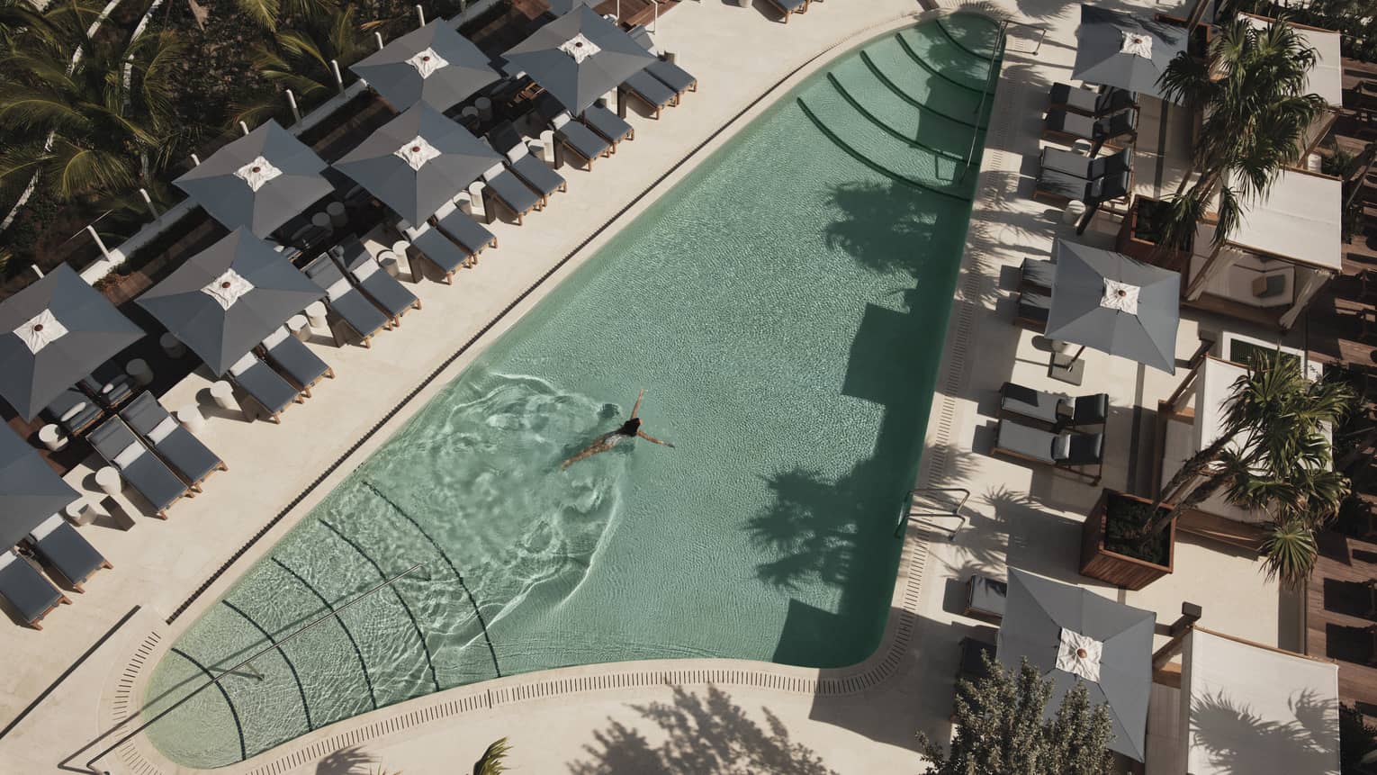 An outdoor swimming pool with grey lounge chairs and umbrellas surrounding it.
