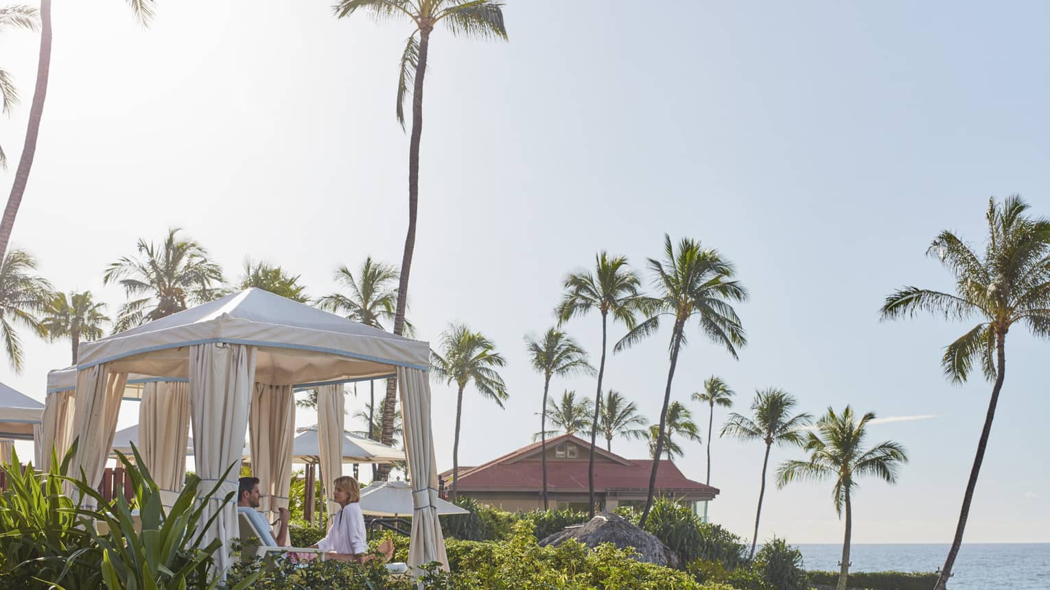Tall palm trees over cabanas with white curtains on sunny day