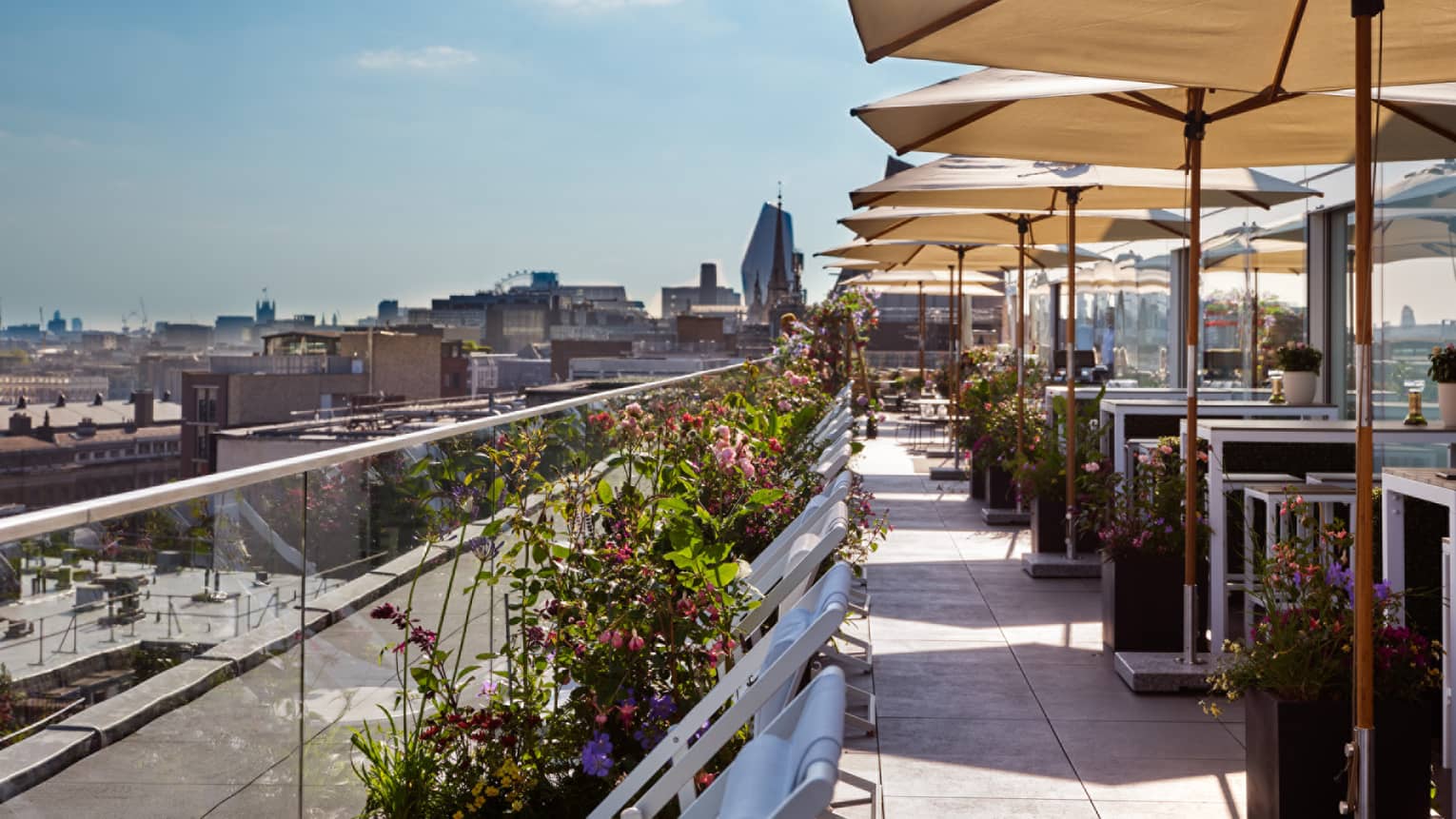 Bloom Lounge terrace with tables and tan umbrellas and flower displays along glass enclosure