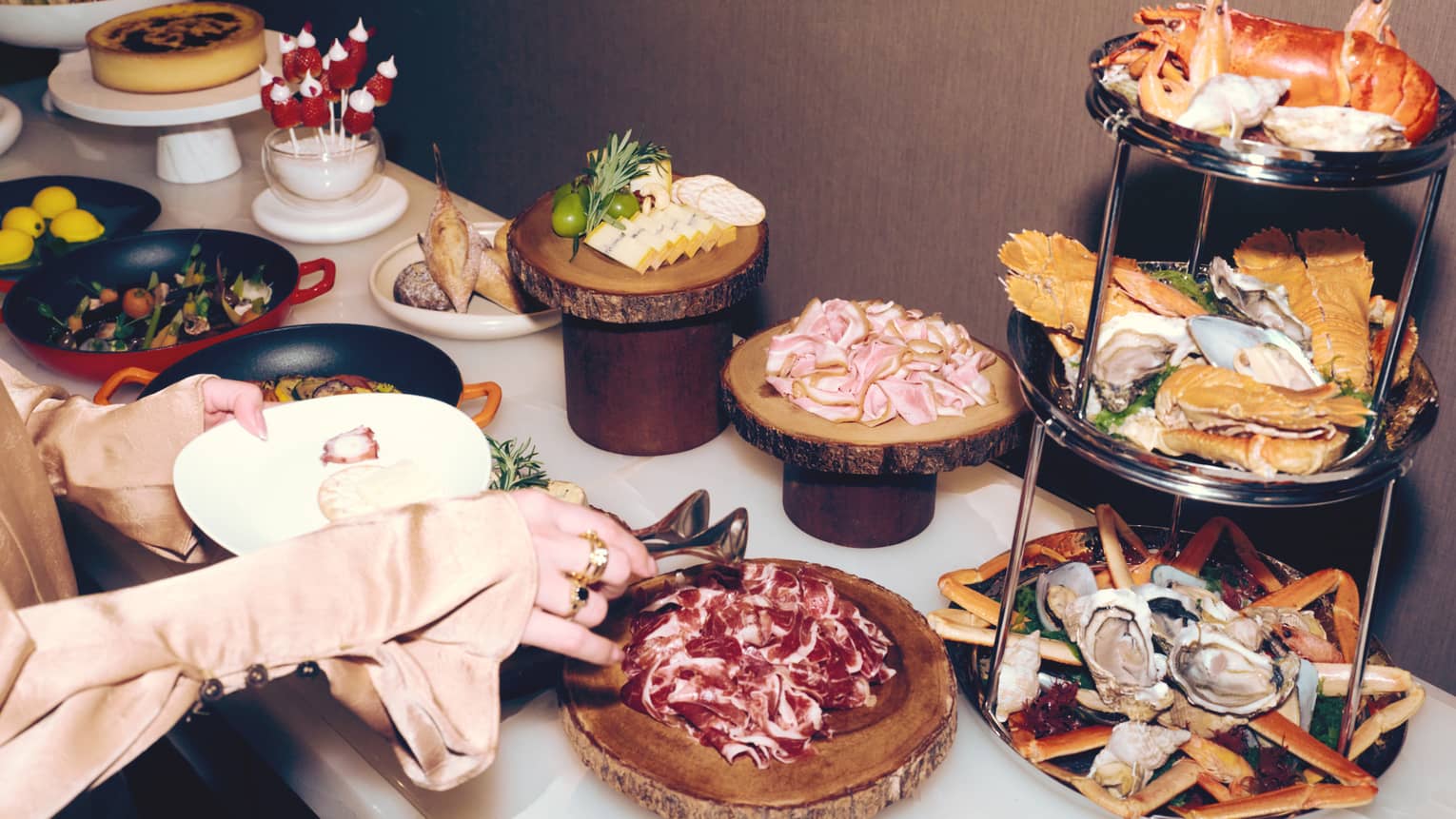 A person makes a plate at a buffet of gourmet food including a three-tier seafood tower