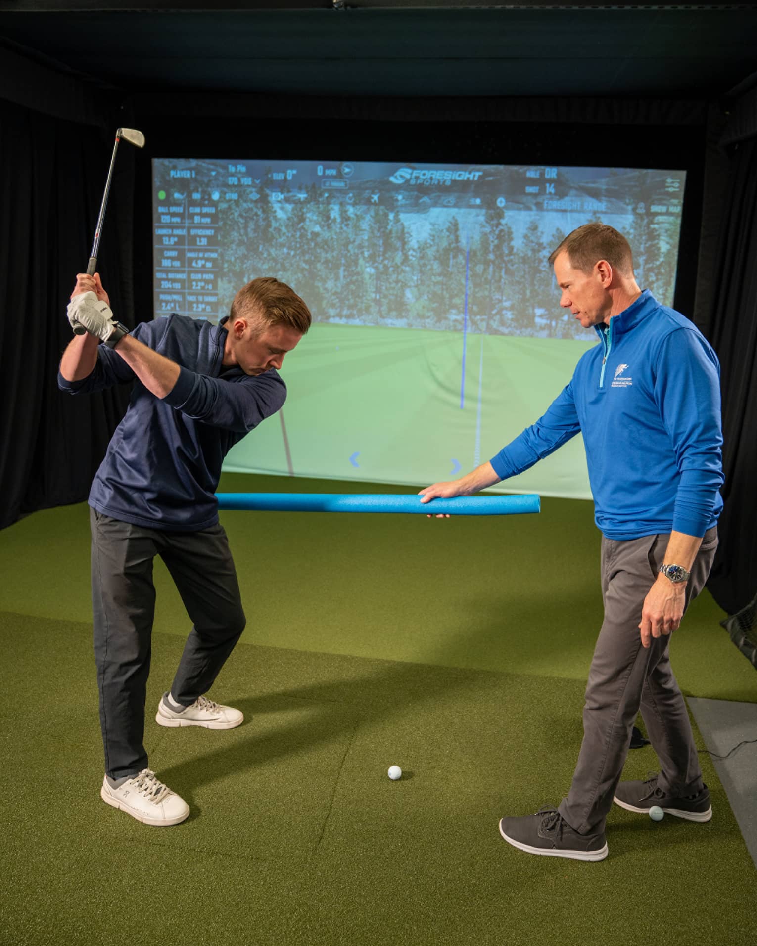 Two guests at a golf simulator, one guest swinging a golf club