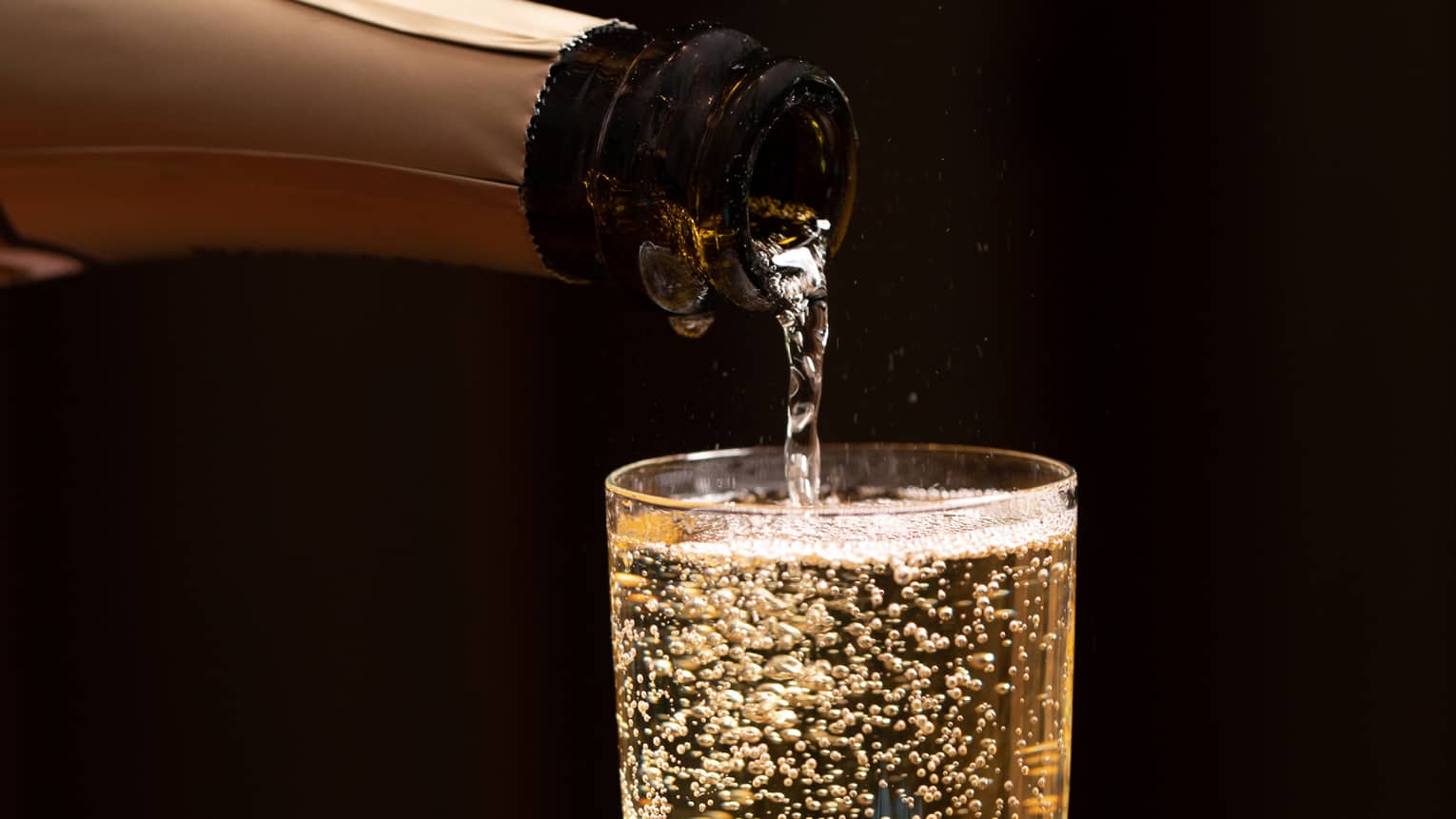 A bottle of champagne is poured into a glass as bubbles float to the top
