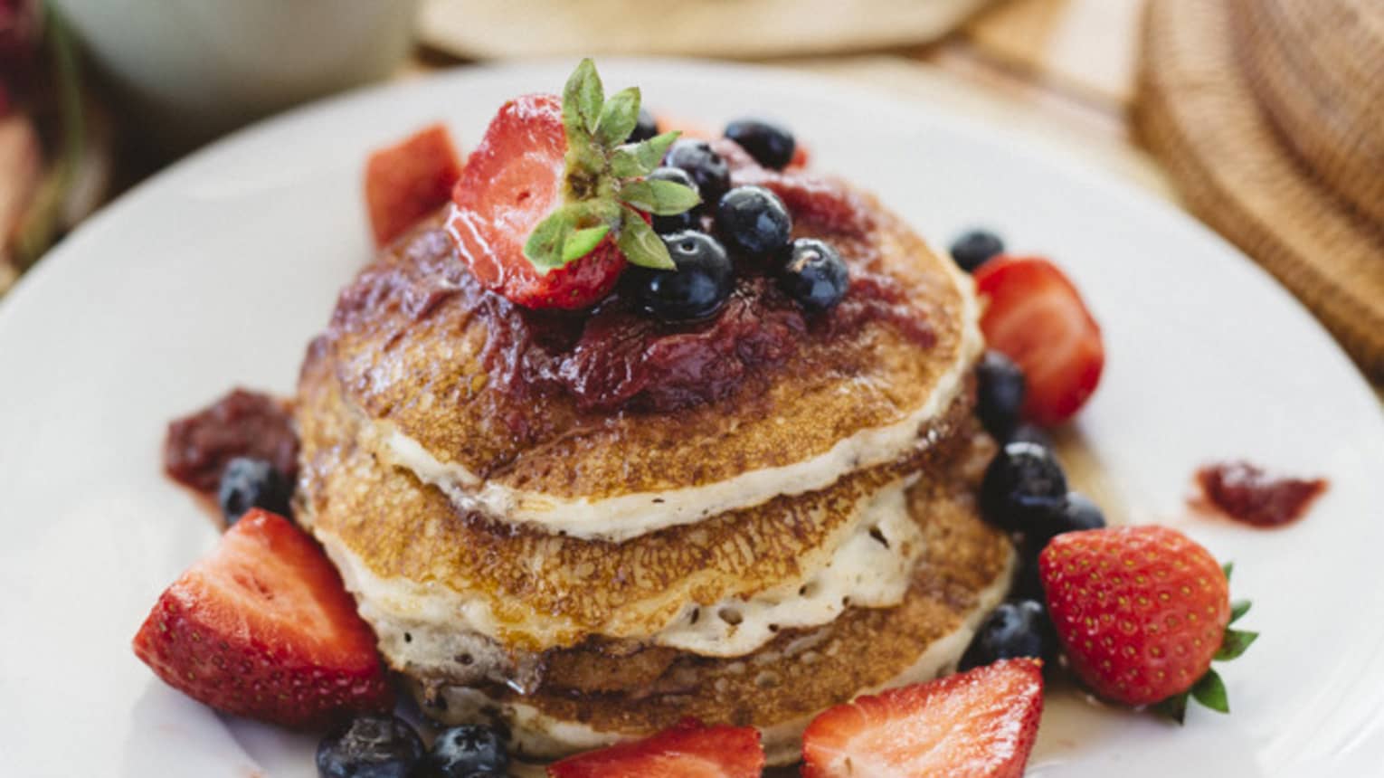 Stack of pancakes with fresh berries on white plate and cup of coffee