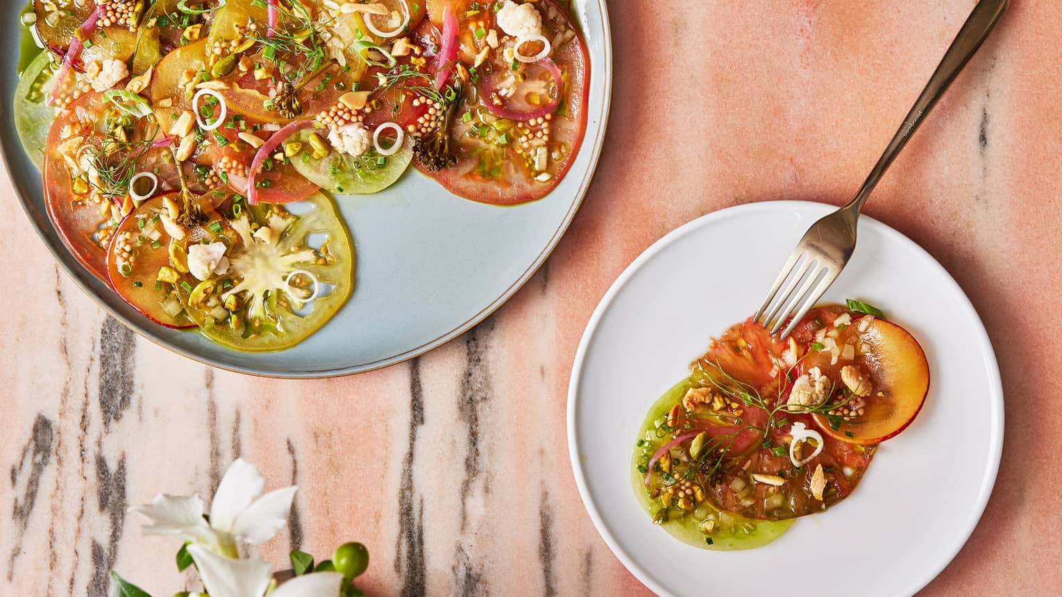 A large and small plate with thinly sliced vegetables and herbs.