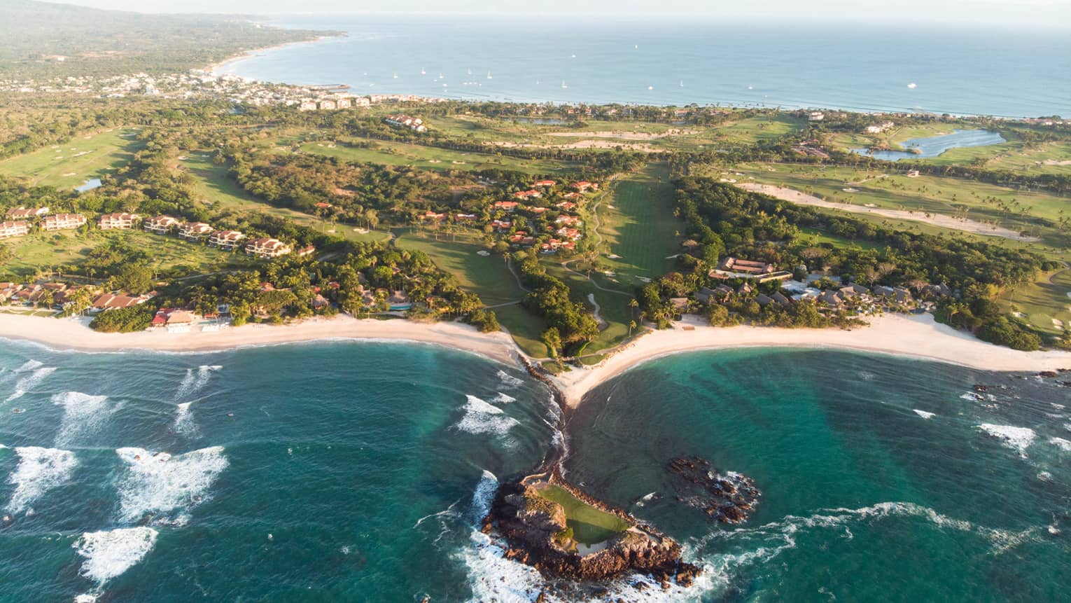 A coastline with deep blue water running up against sand and plants.