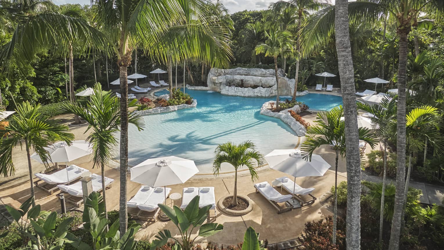 Luxury resort pool surrounded by palm trees, white lounge chairs and large umbrellas