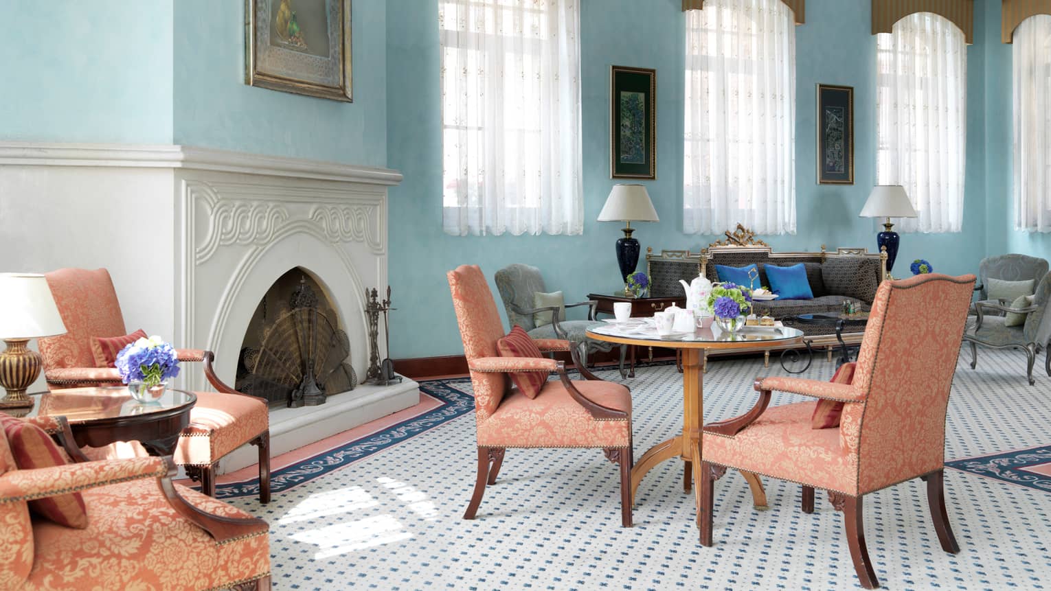 Dining area with light blue walls, windows, salmon-coloured upholstered chairs at small wood, round tables