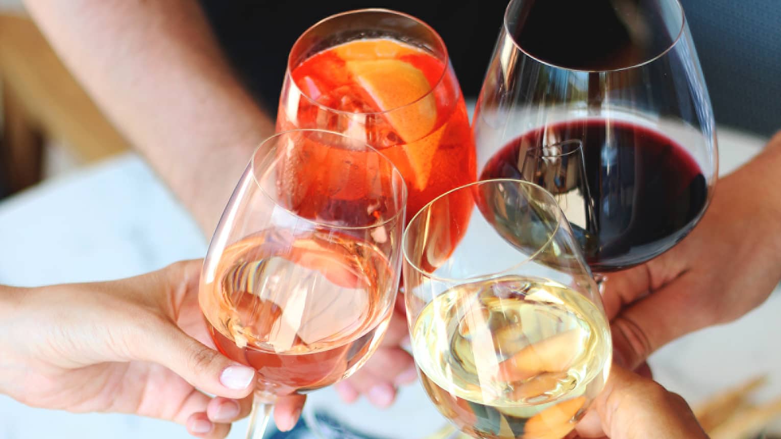 Four hands toasting with different kinds of wine above charcuterie platter