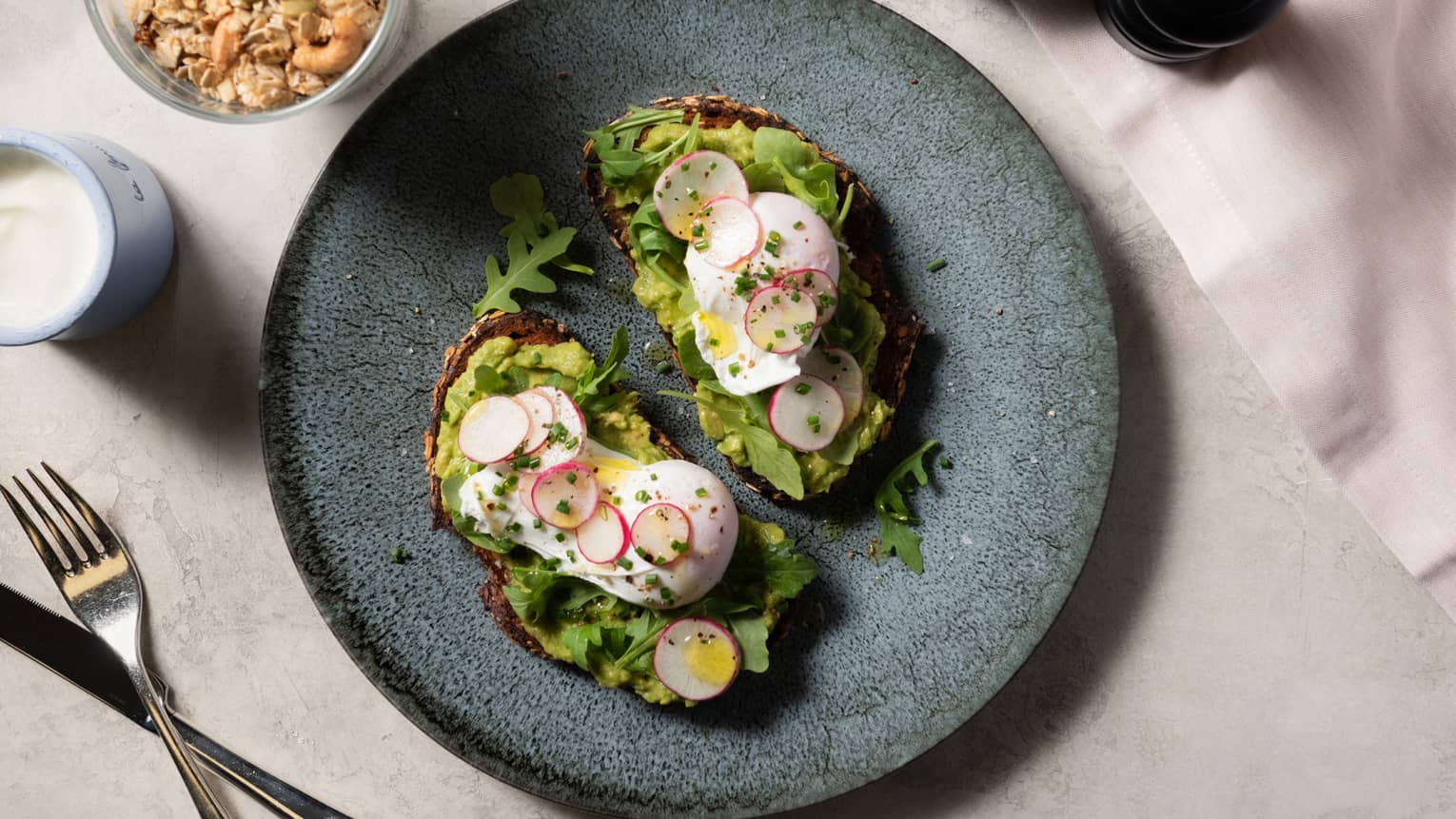 Eggs and avocado toast on a blue plate next to granola.