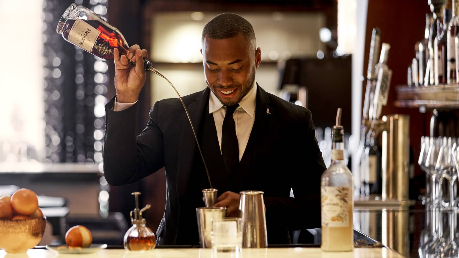 A bartender pouring a drink into a shaker.