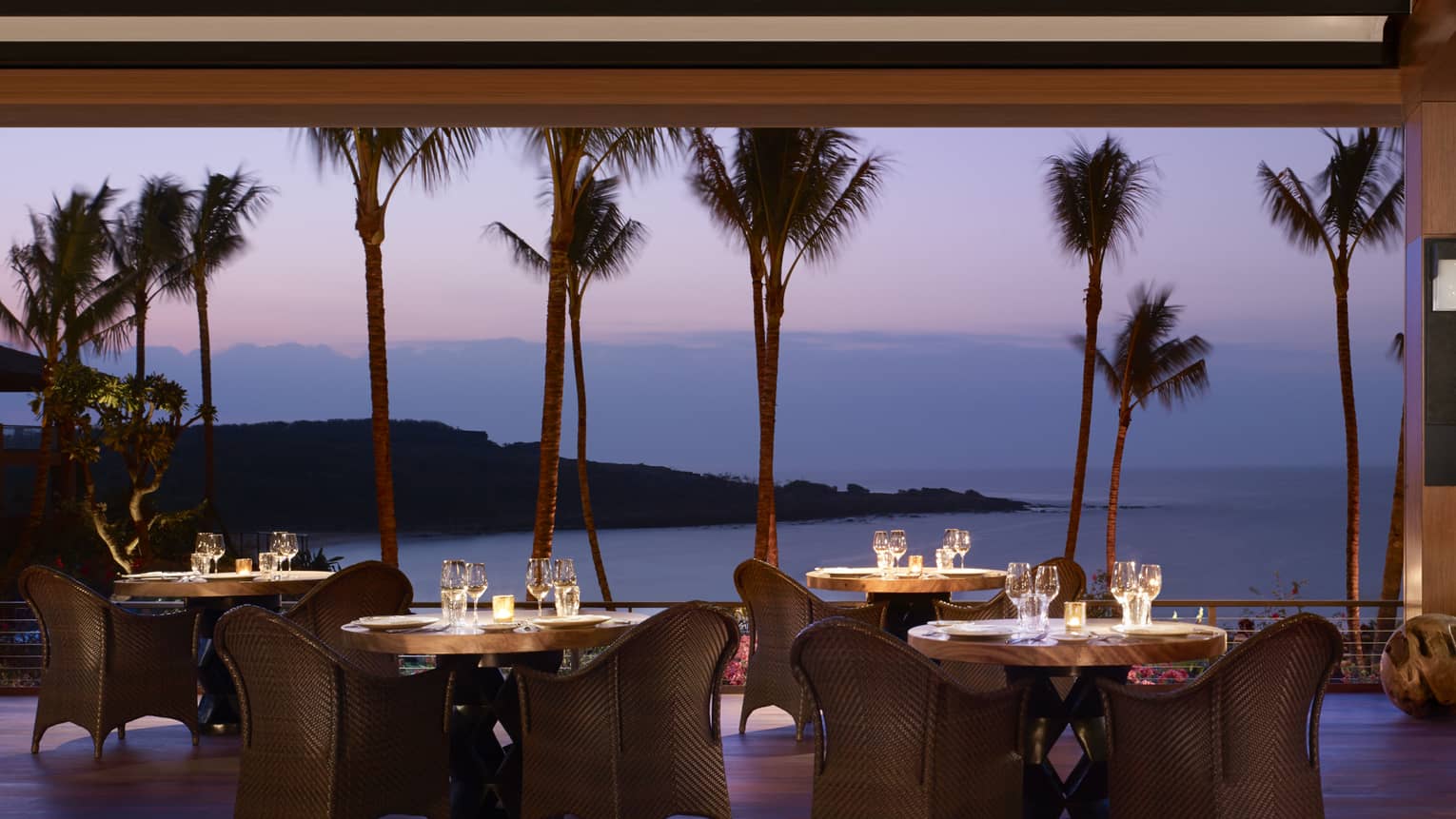 Wicker dining chairs around patio tables overlooking beach on One Forty patio at night