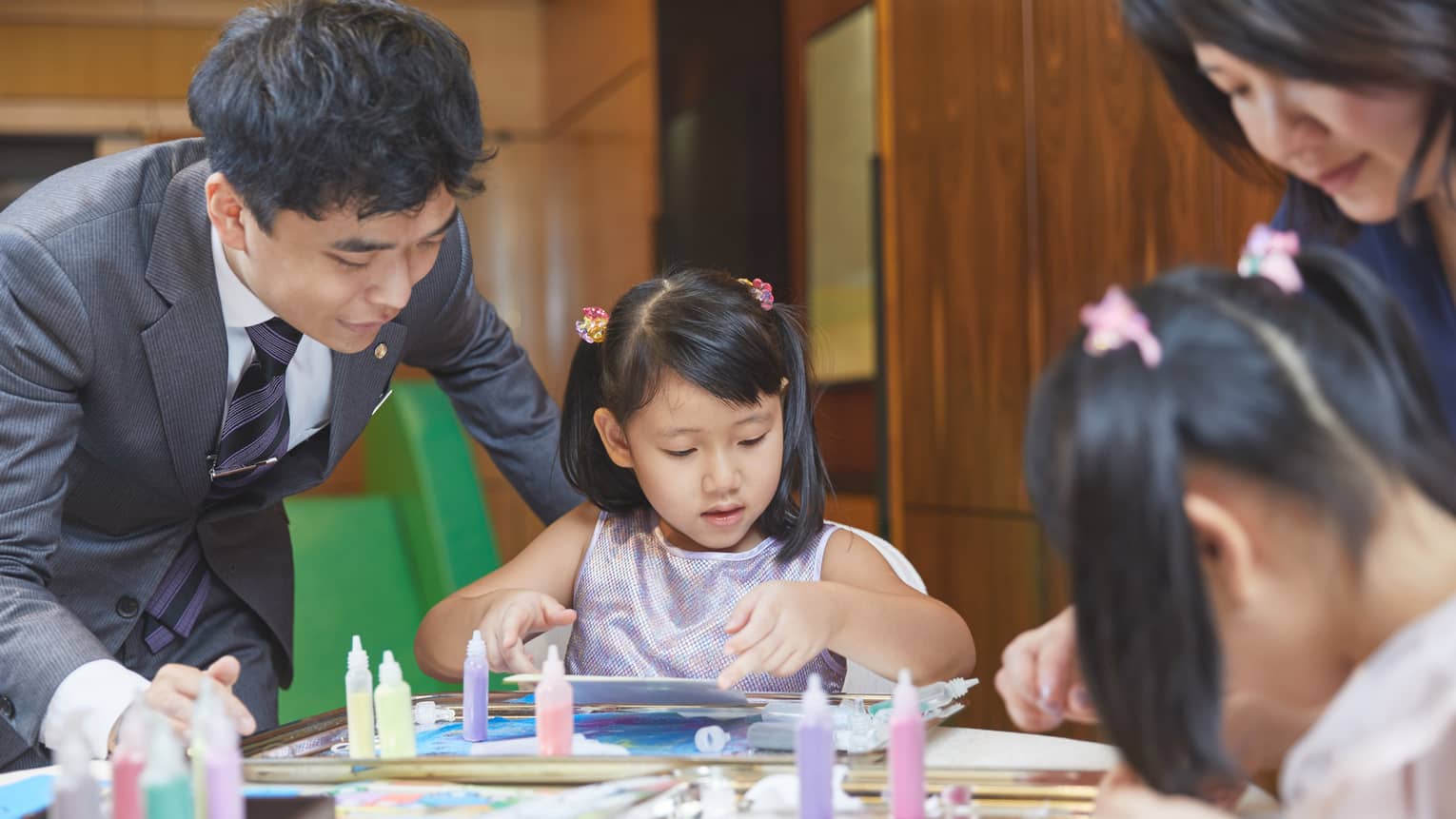 Twi young girls doing art with parents or property team members guiding them.