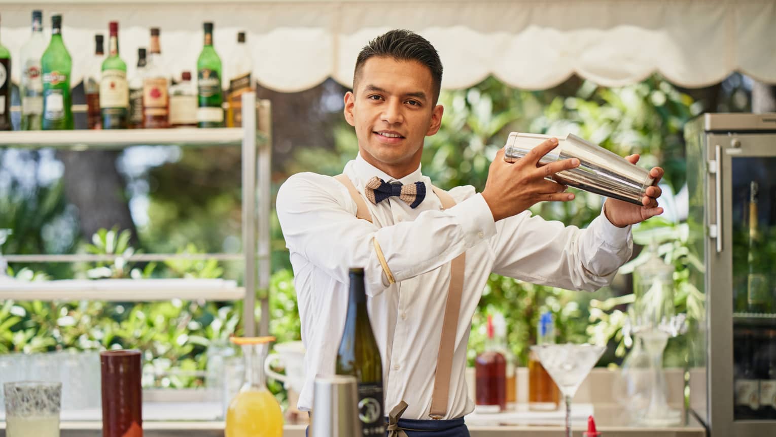 Barman Frank Carcamo standing behind outdoor bar, shaking a cocktail