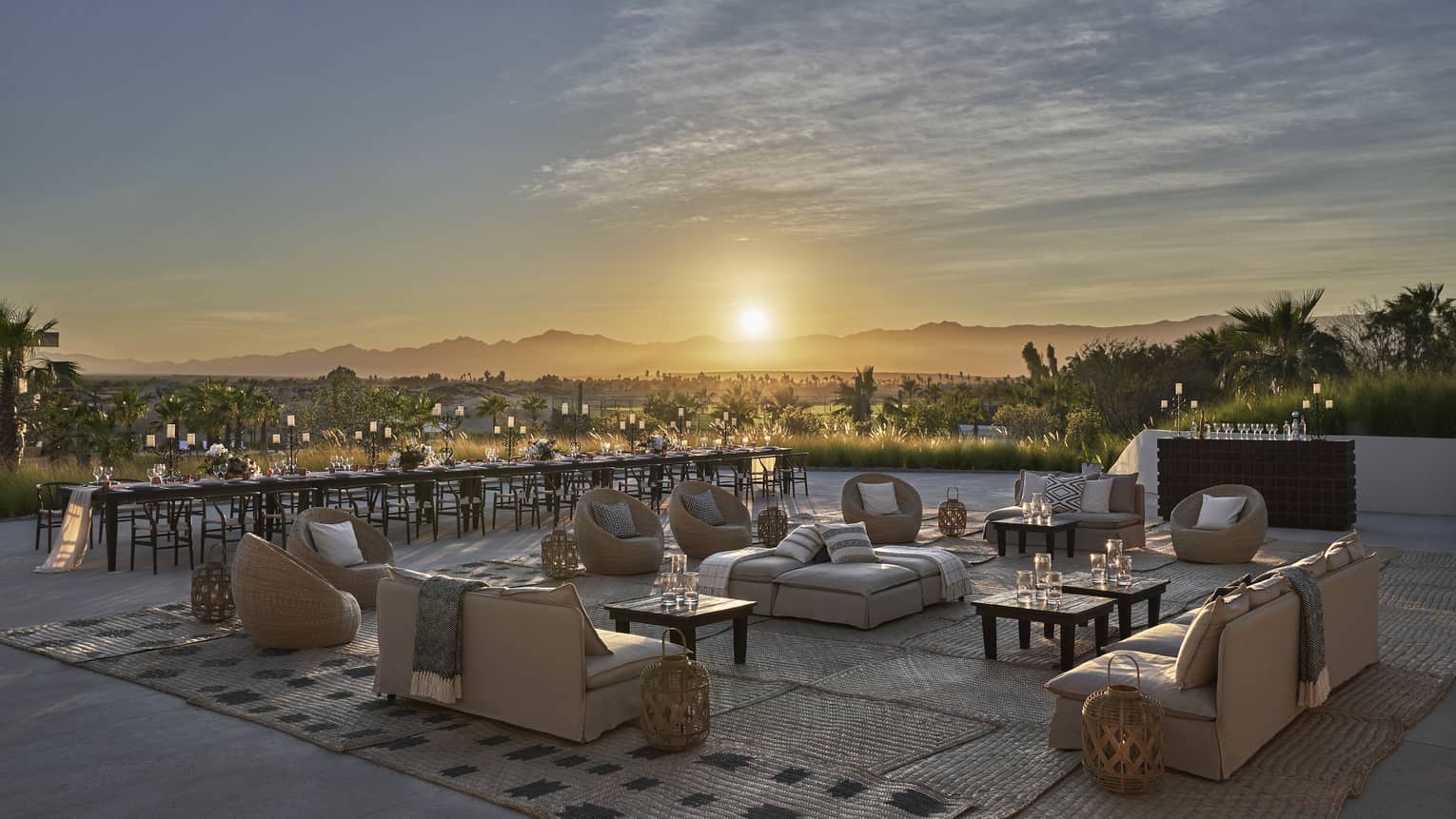 The sun sets beyond the open air ballroom terrace furnished with low cream colored couches and low dark wooden tables overlooking los cabos 