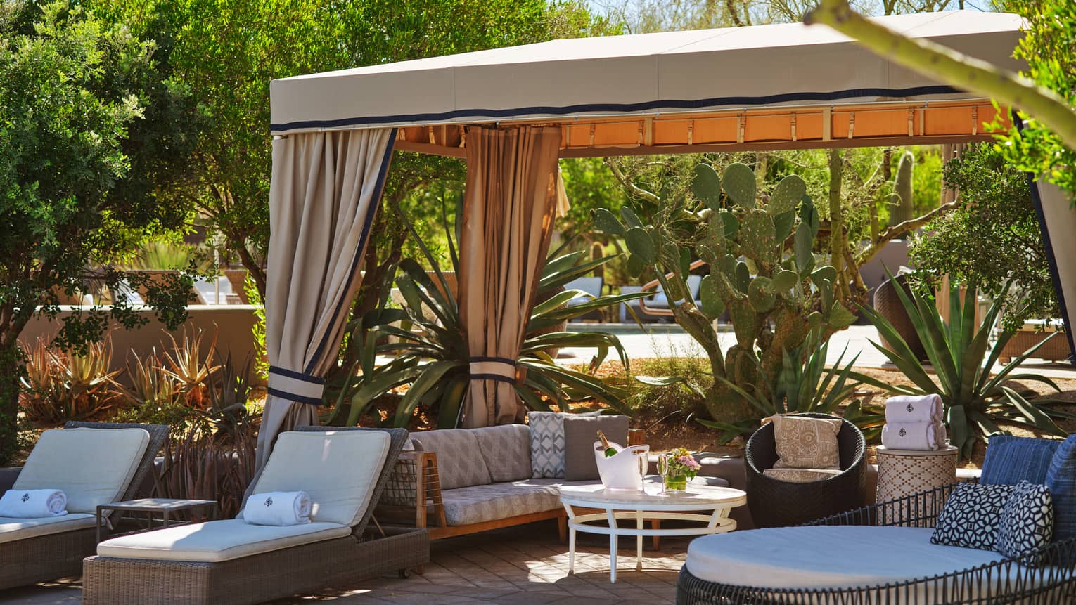 Cabana with lounge chairs, a couch, table and trees surrounding it.