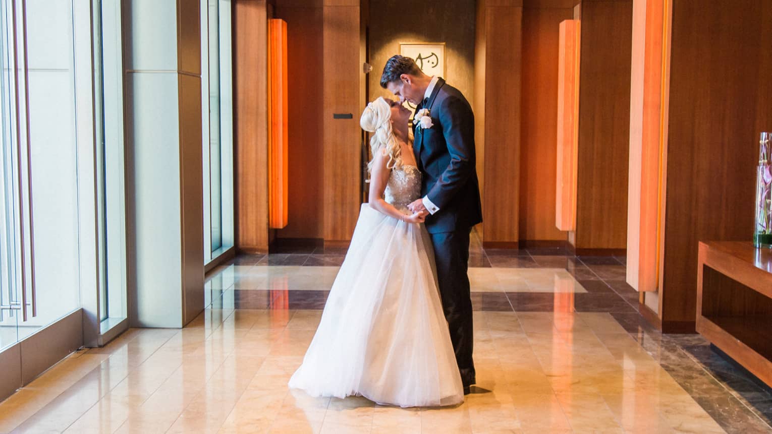 Bride and groom embrace in bright hotel hallway