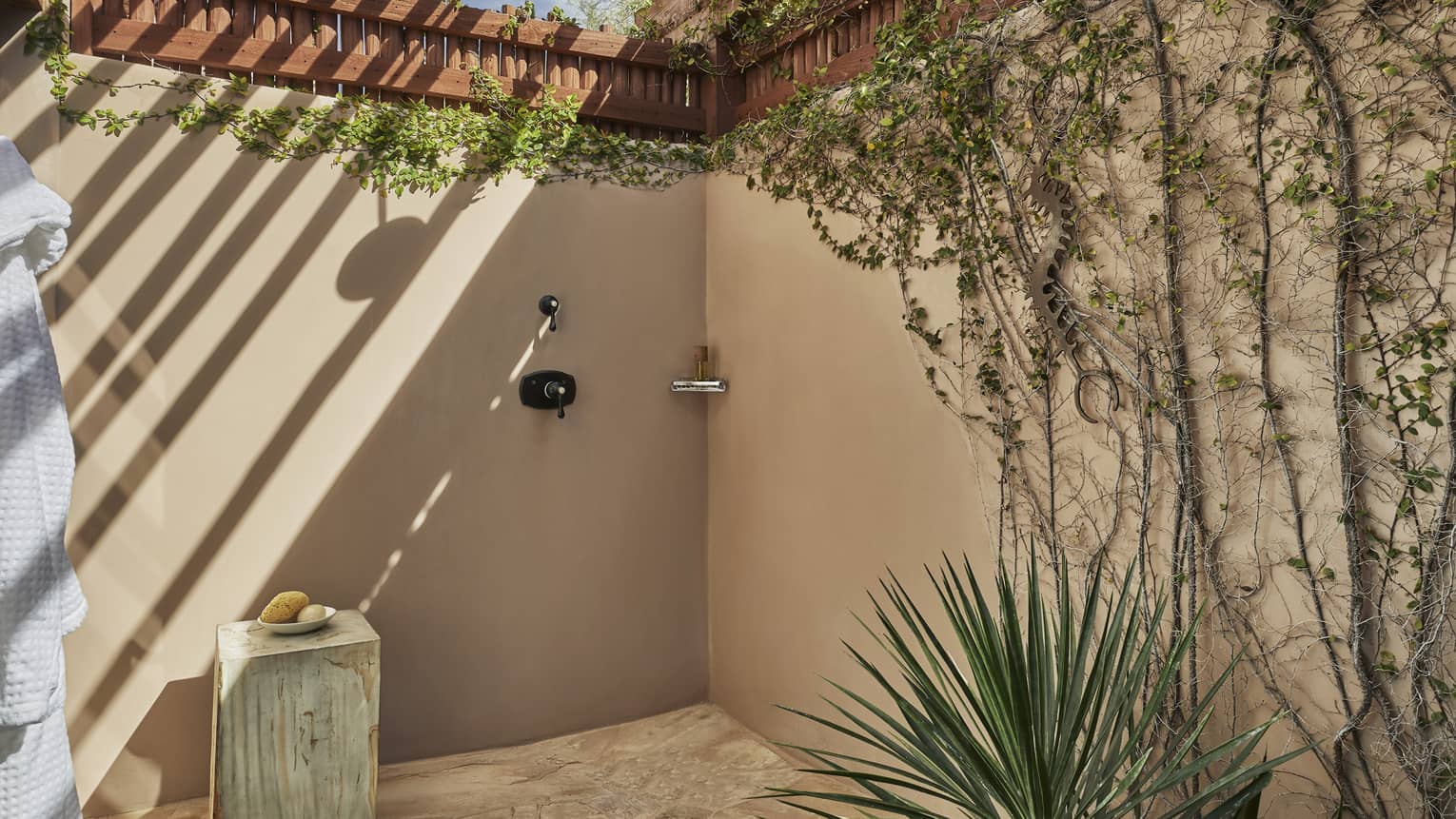 Stucco outdoor shower with creeping vines on the wall, covered by portico