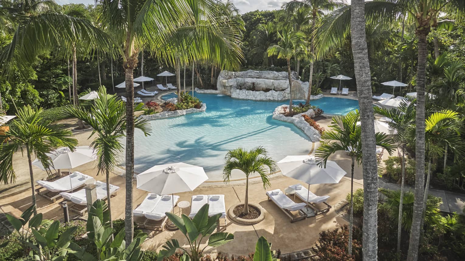 Luxury resort pool surrounded by palm trees, white lounge chairs and large umbrellas
