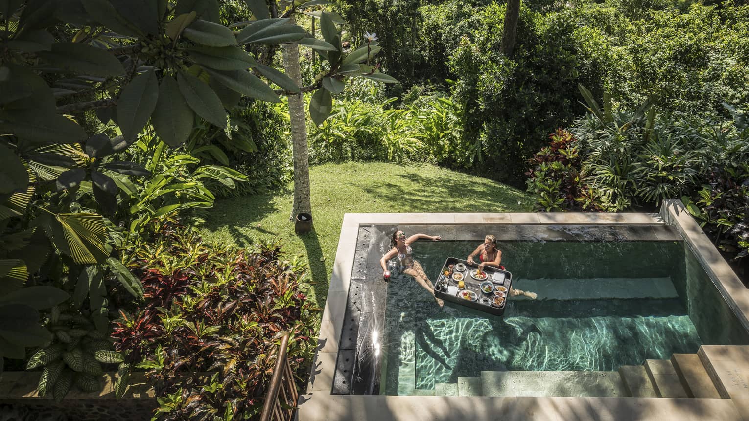 A couple lounges in the pool with breakfast on a floating tray 