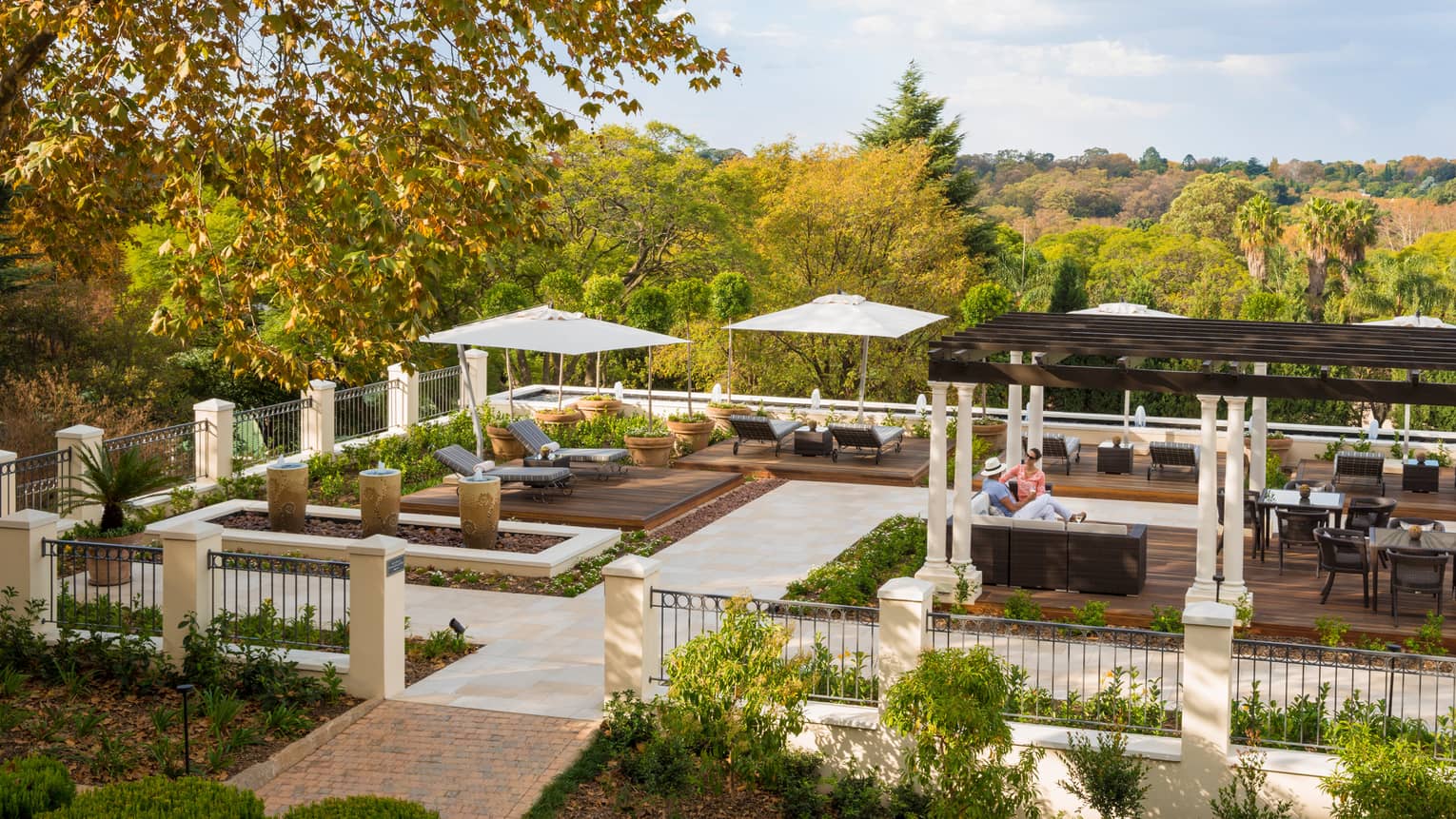 Looking down at iron fence around outdoor patio and courtyard with lounge chairs, people under pergola