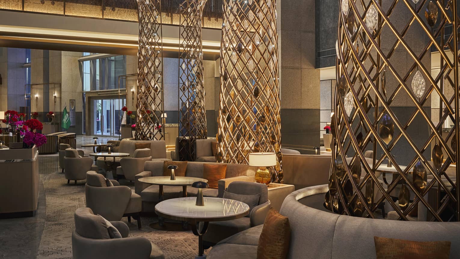 Hotel lounge with towering ceilings, large connical metal tree sculptures surrounded by plush seating and various tables and chairs