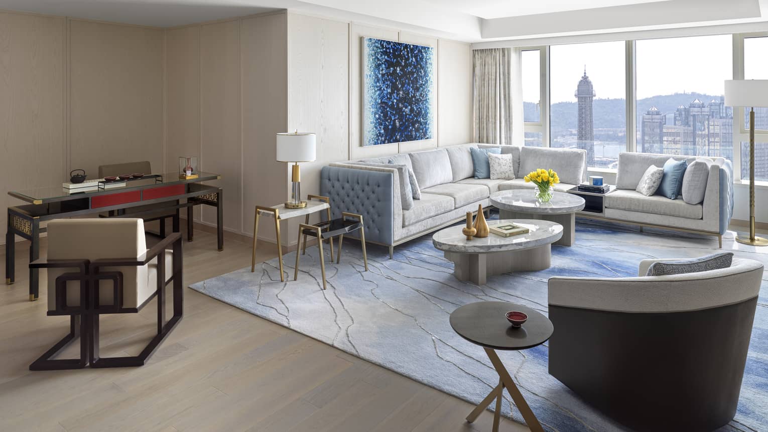 Imperial Suite with white leather sectional, marble nesting tables, dining table, accent chair, blue decor, floor-to-ceiling window with city views