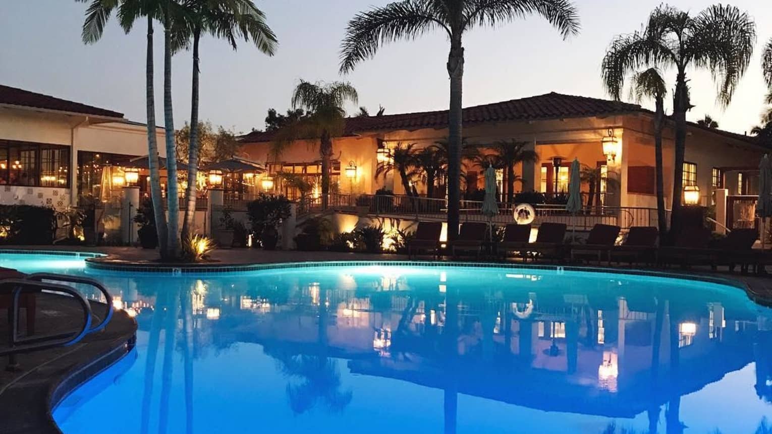Hotel lights reflected in blue swimming at dusk, silhouettes of towering palm trees