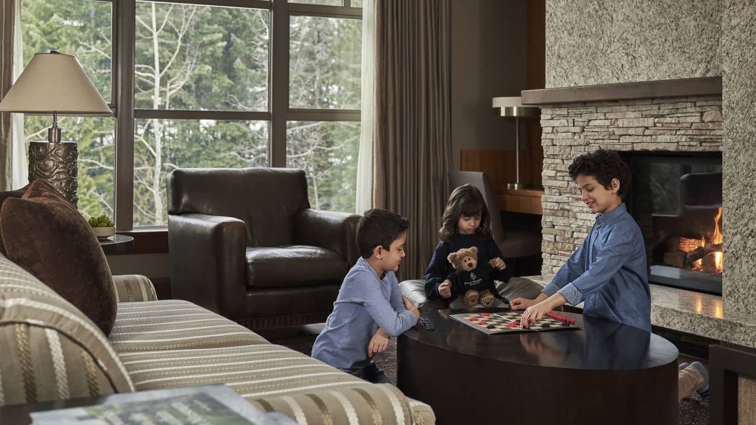 Three children play a game of checkers in front of a roaring fire within the living room of their suite.