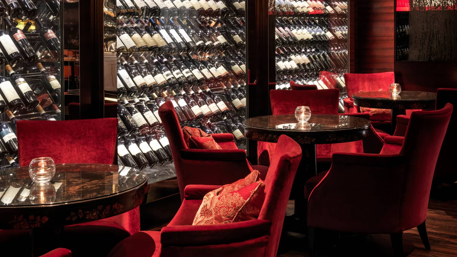 Close-up of Amaranto Bar red velvet lounge chairs by glass cellar, bottles