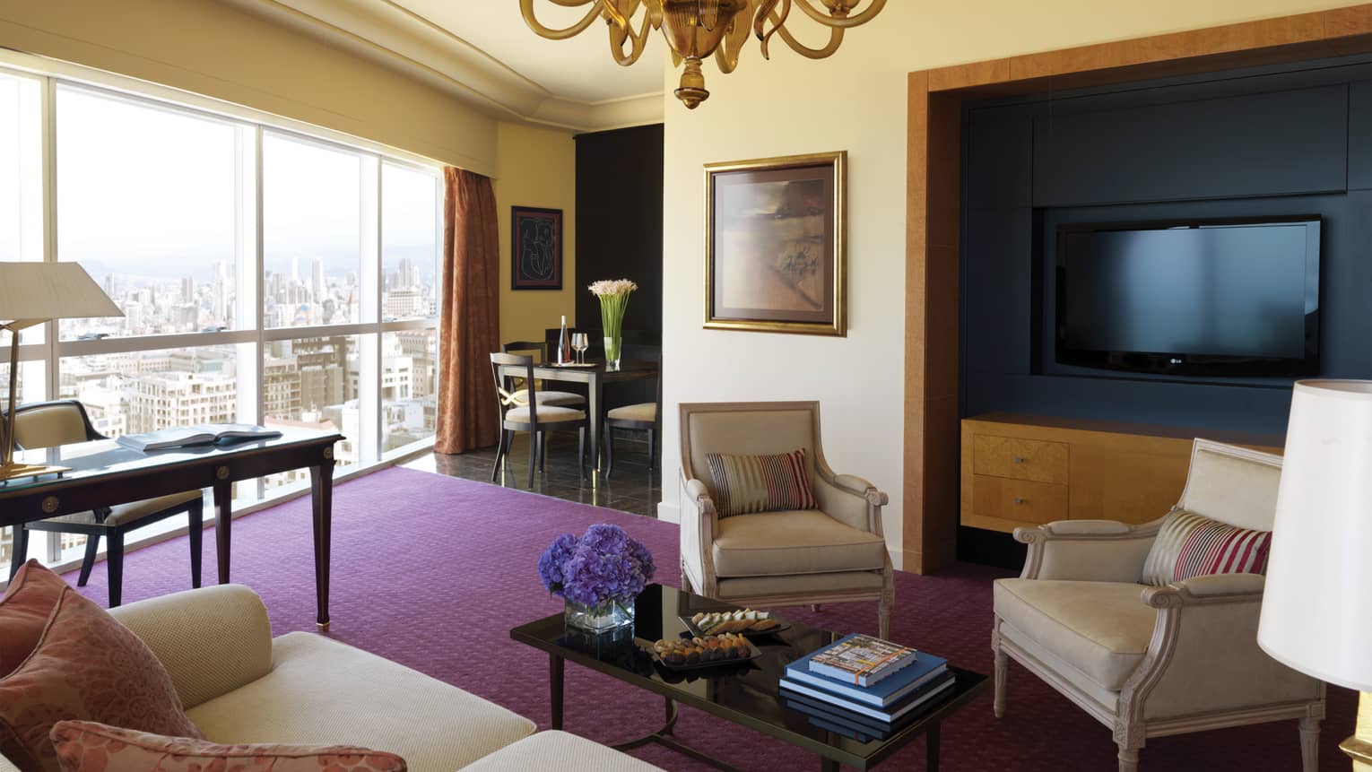 Residential Suite living room with sofa and two chairs, coffee table, purple carpet, large TV, dining table in view