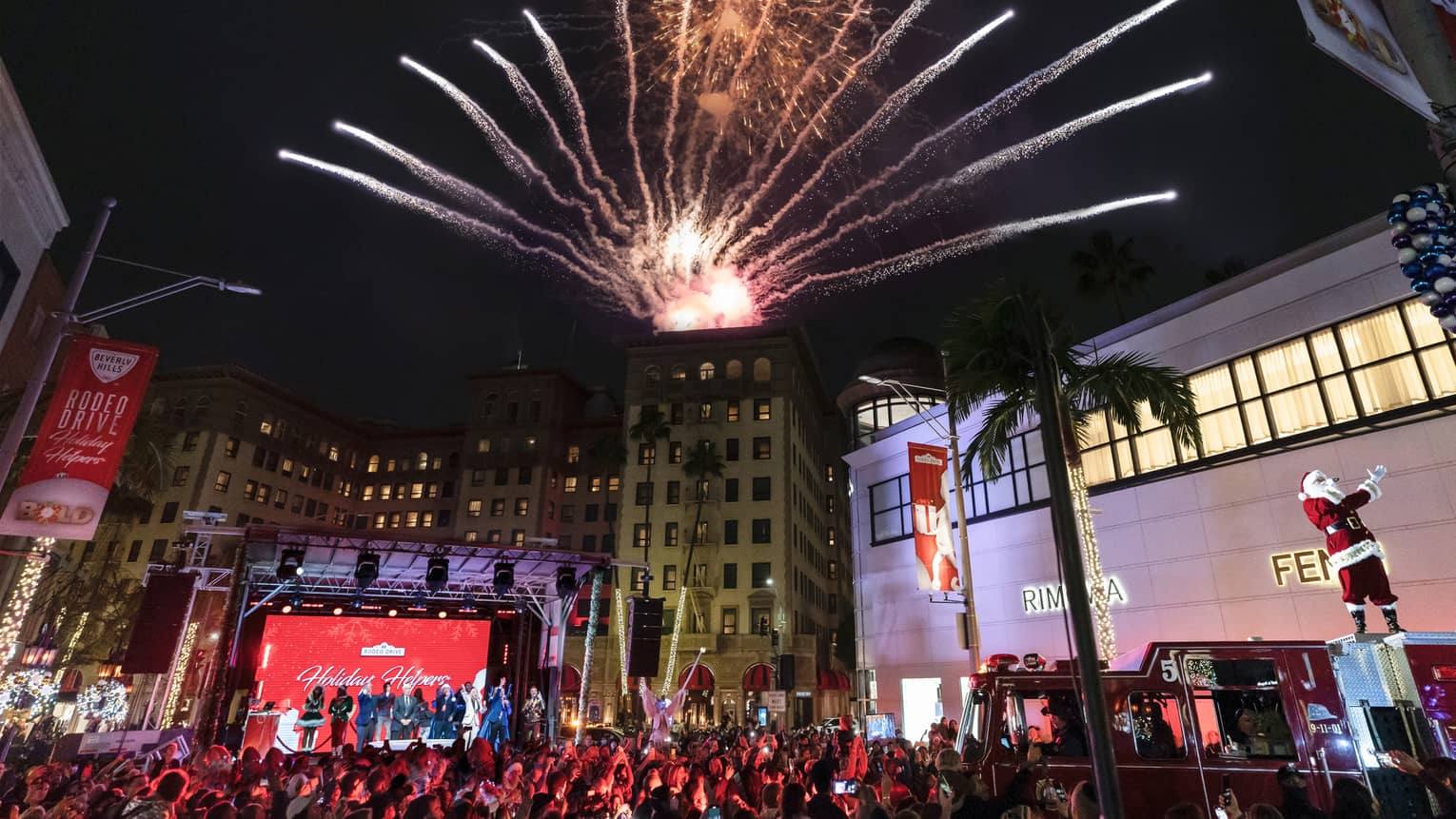 Fireworks exploding over buildings and large crowd during the holiday season.