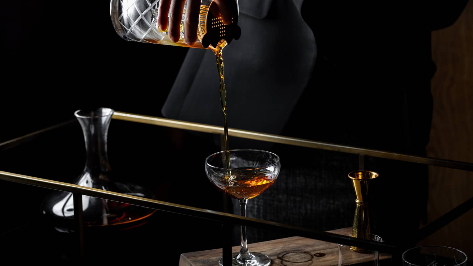 Close-up of bartender pouring drink from crystal cocktail shaker in dark bar 