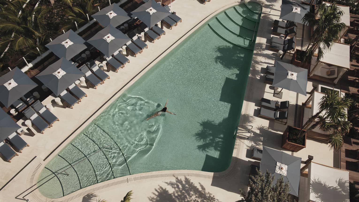 An outdoor swimming pool with grey lounge chairs and umbrellas surrounding it.