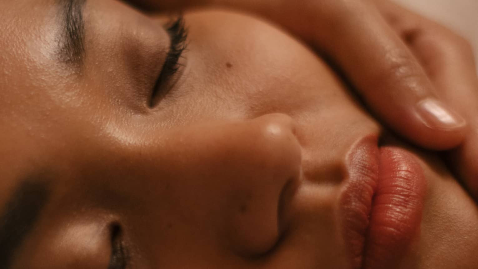 Closeup of hands on either side of woman’s face during facial