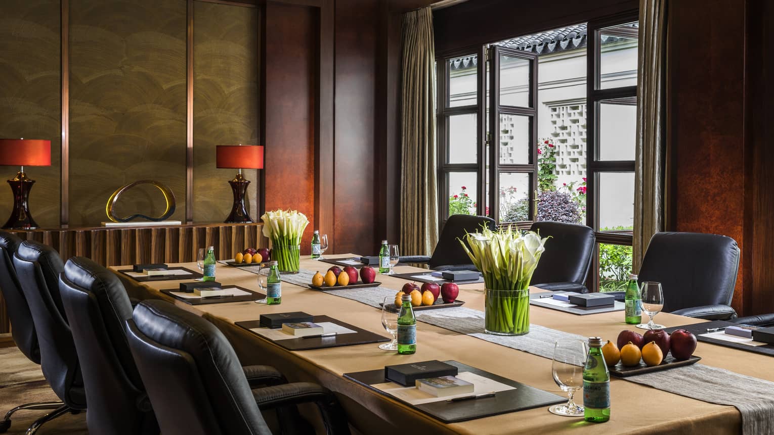 Large boardroom meeting table lined with leather executive chairs, glass patio door
