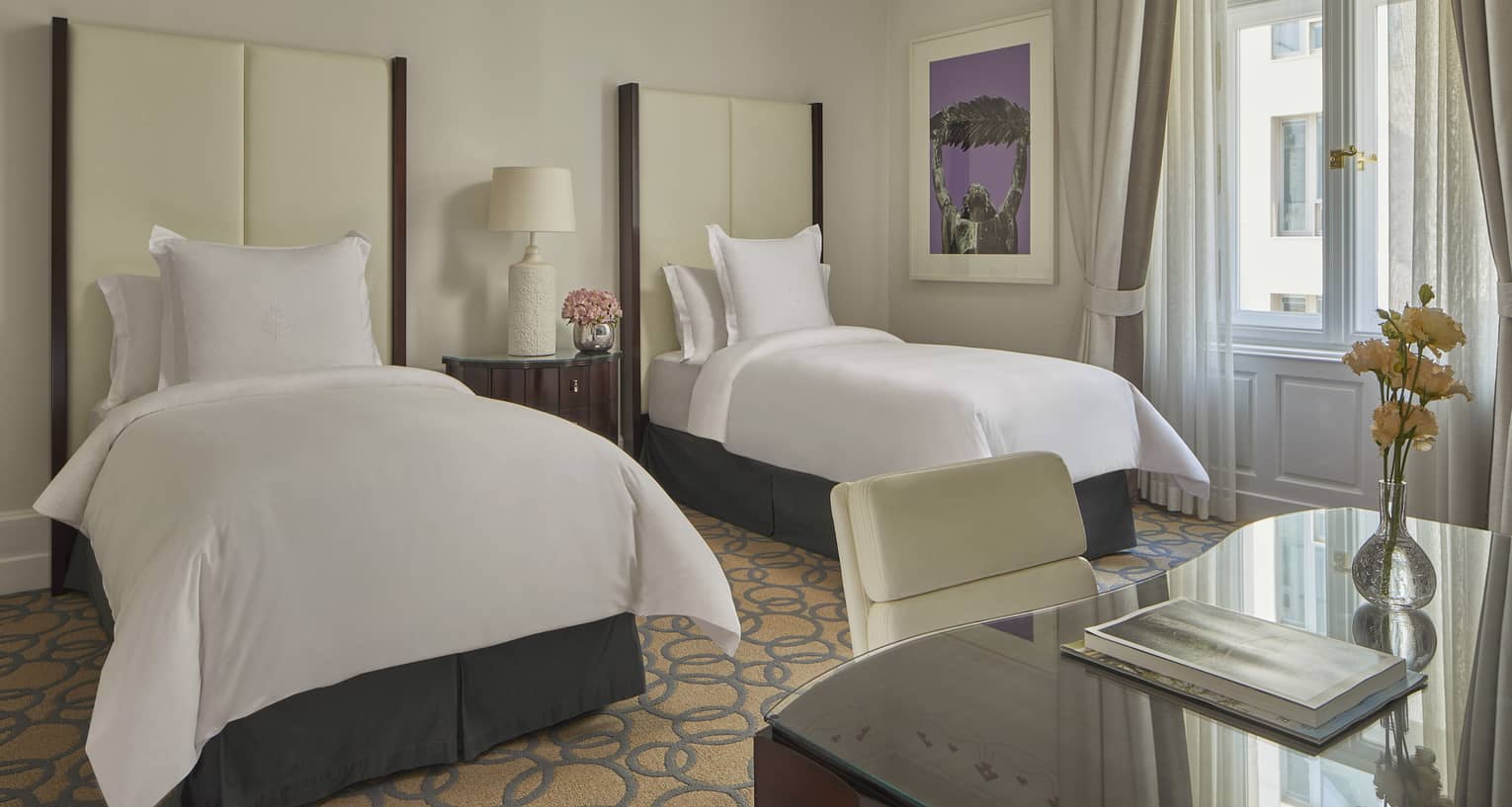Room with two white twin beds with tall headboards and desk with chair