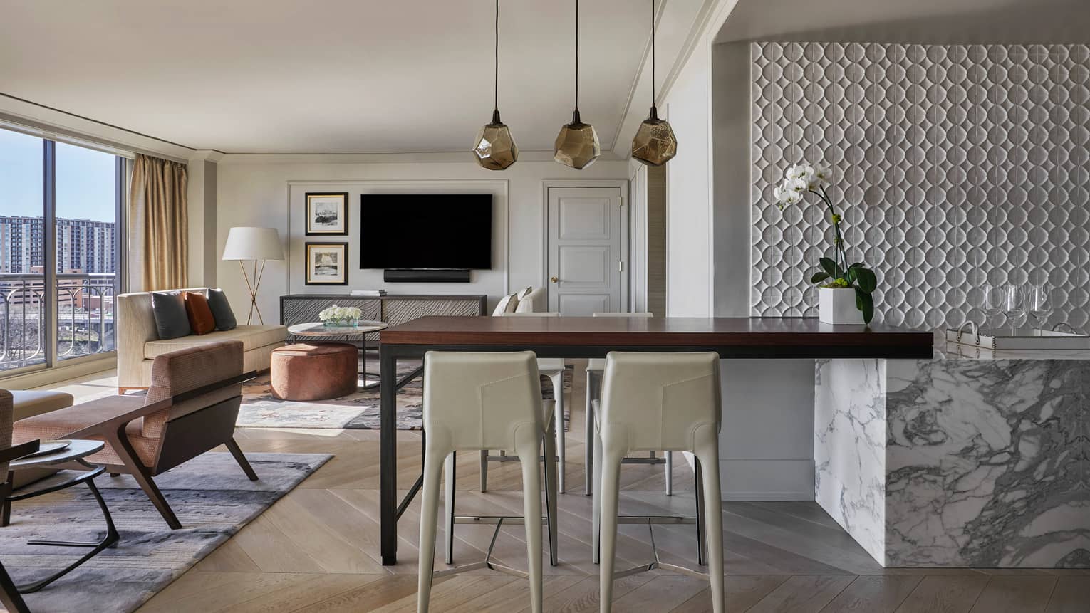 Governor's Suite white stools at tall wood table, three modern hanging lights, bright living room