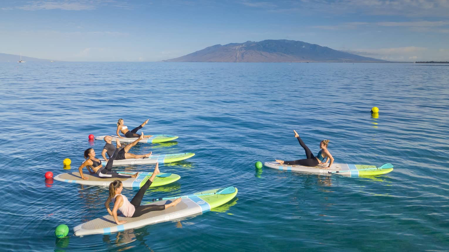 Five people float on surfboards on ocean, lift legs in fitness pose