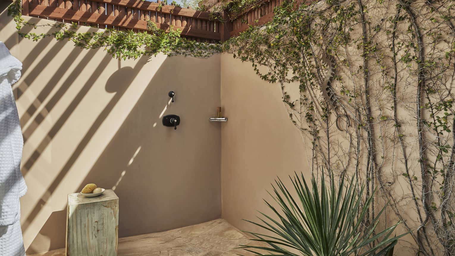 Stucco outdoor shower with creeping vines on the wall, covered by portico