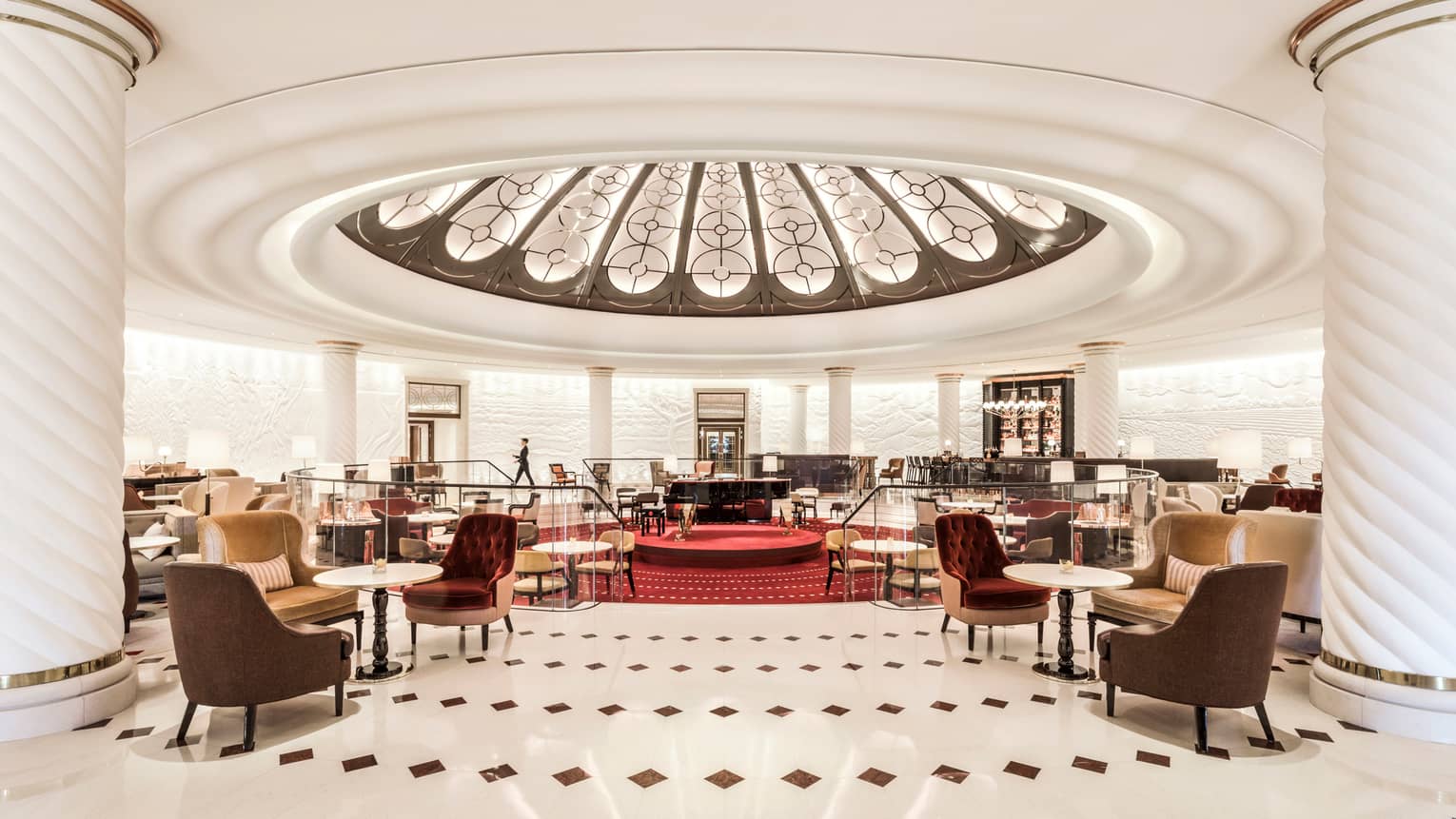Rotunda bar cocktail tables and chairs around sunken lounge with red carpets, grand piano, dome ceiling