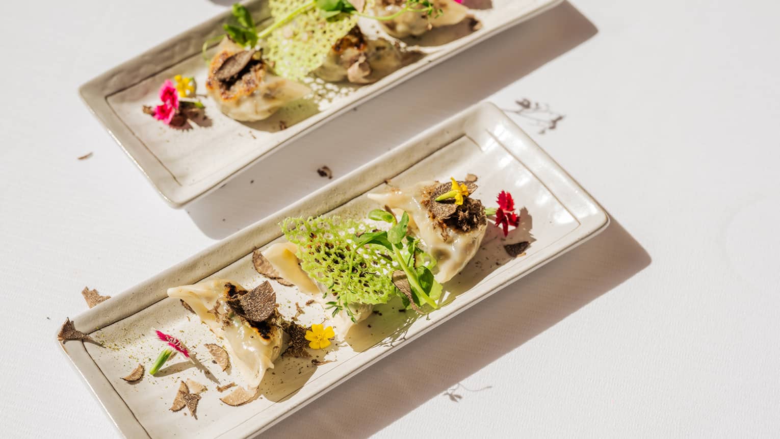 Two platters of gyoza with greenery served on a white table.