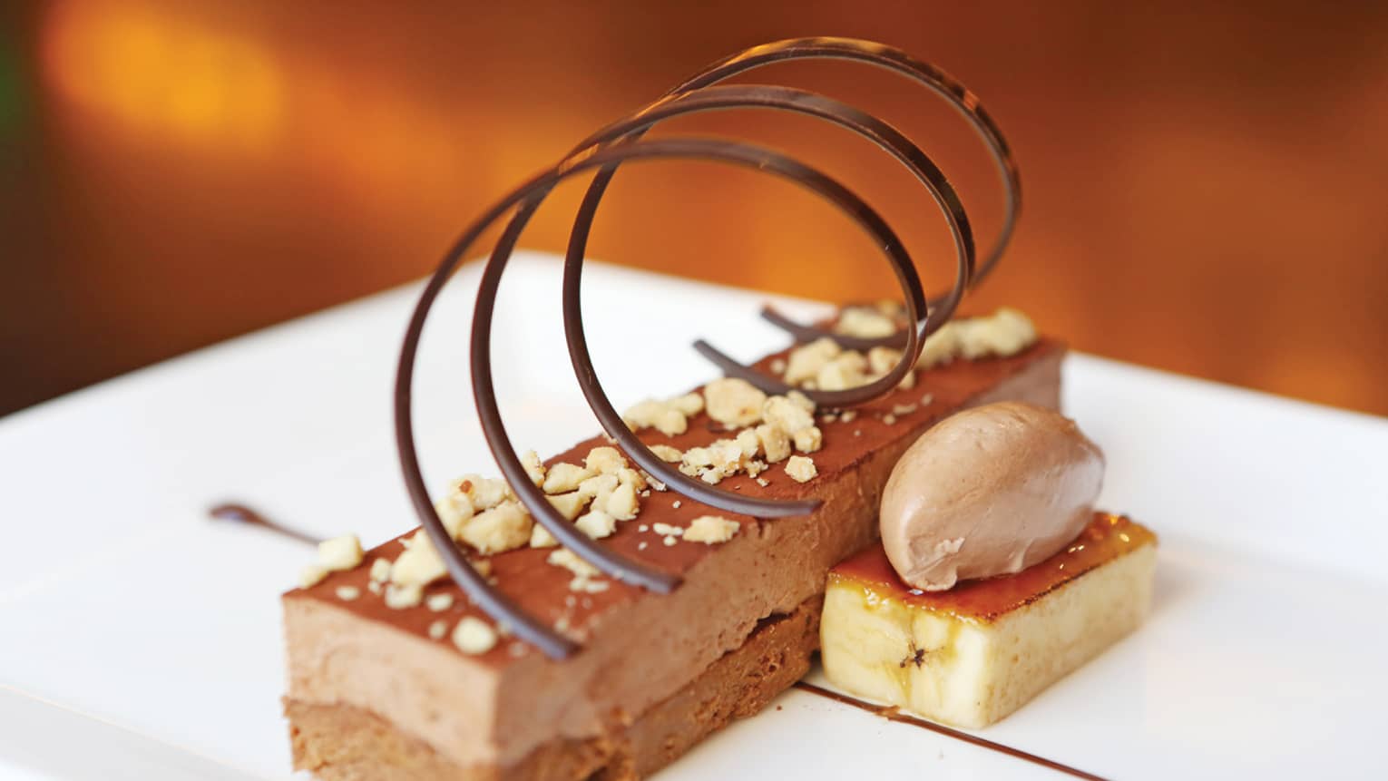 Long slice of Peanut Butter Crunch cake topped with crushed peanuts, spiral chocolate garnish