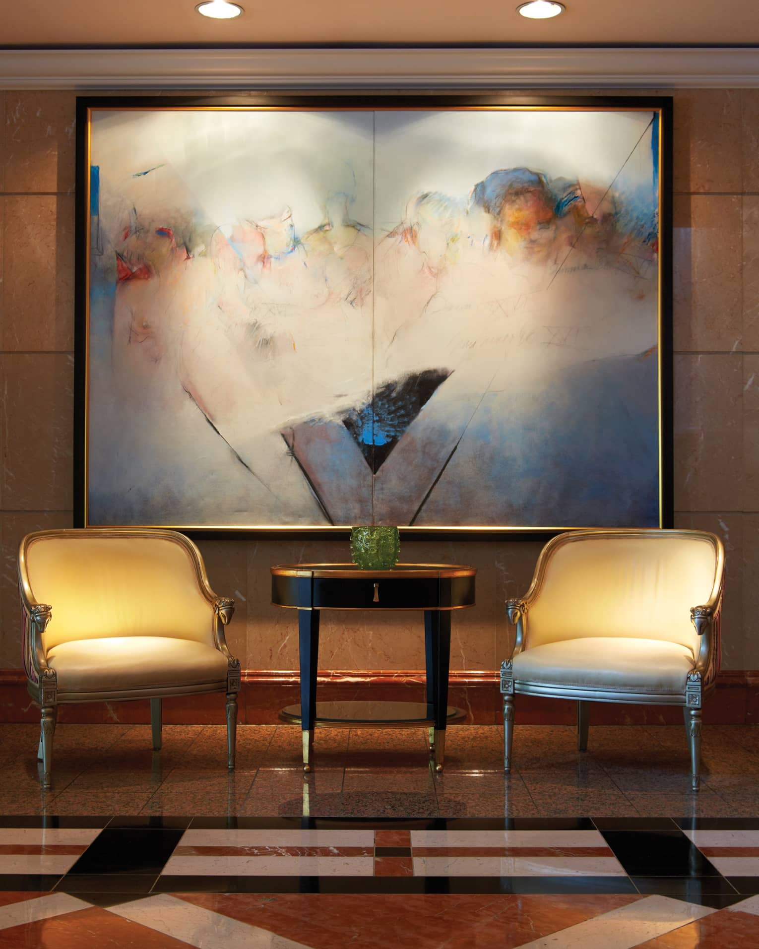 Two Art Deco-style armchairs with gold trim beside table under large abstract painting