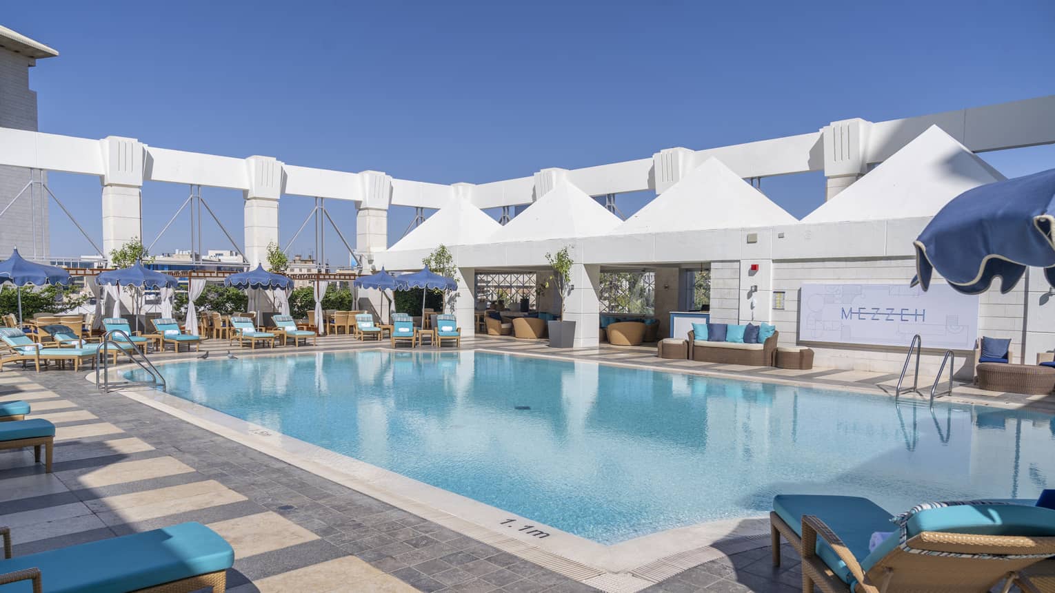 Outdoor pool surrounded by blue lounge chairs and four white tents