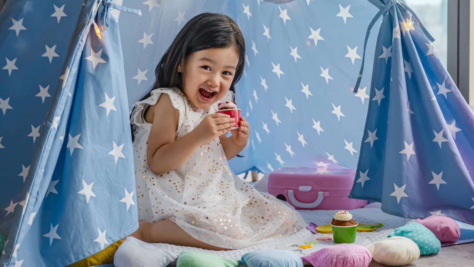 Smiling child playing with toys in a star-patterned tent