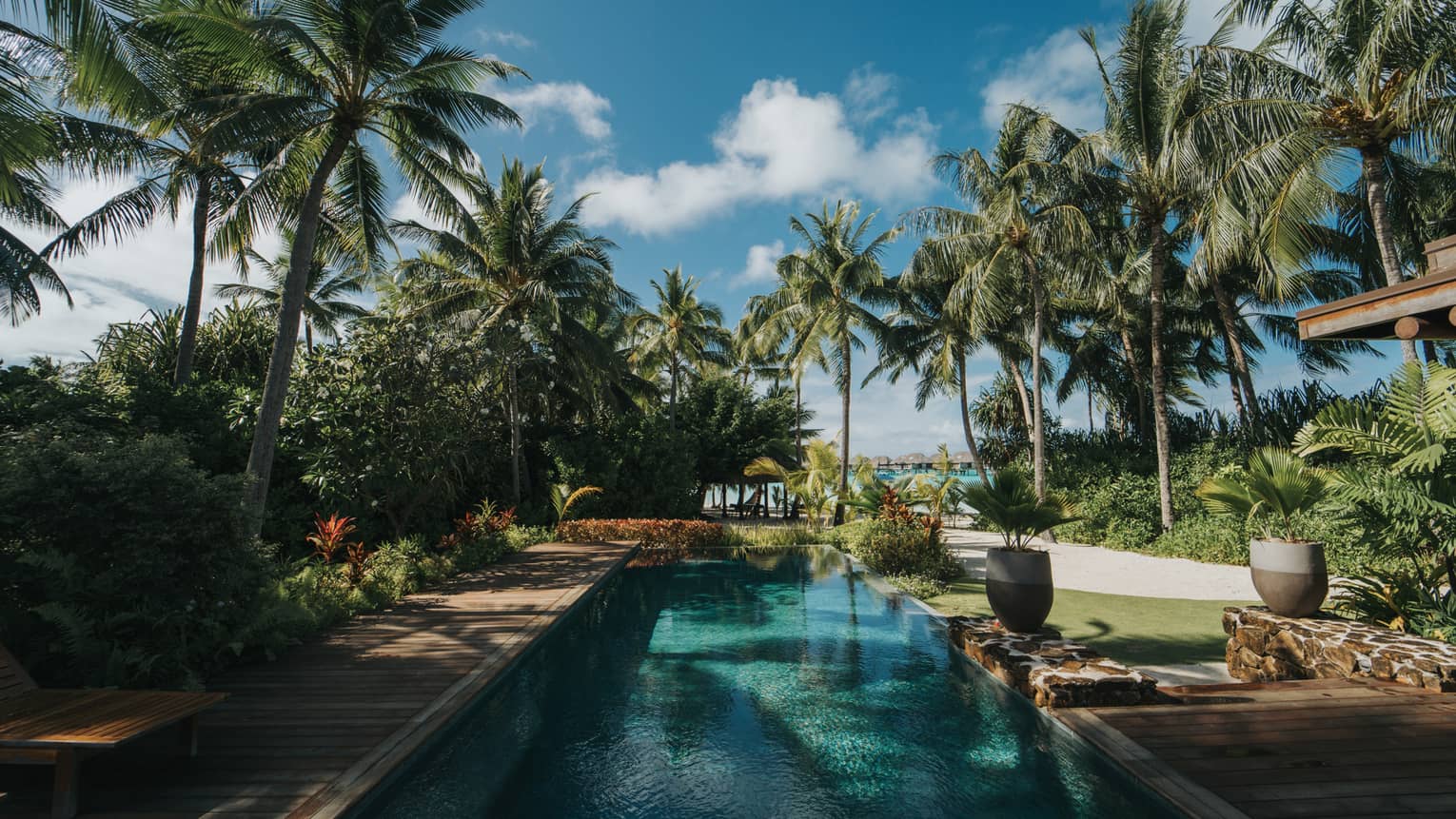 Pristine lap pool of the One-Bedroom Beachfront Villa Estate flanked by palm trees on either side; blue skies and fluffy white clouds 