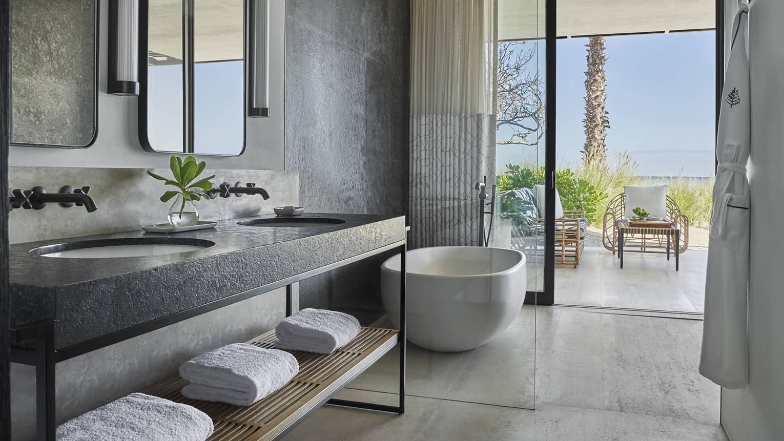 A bathroom with a large sliding glass door, bathtub, sink and towels on a shelf.